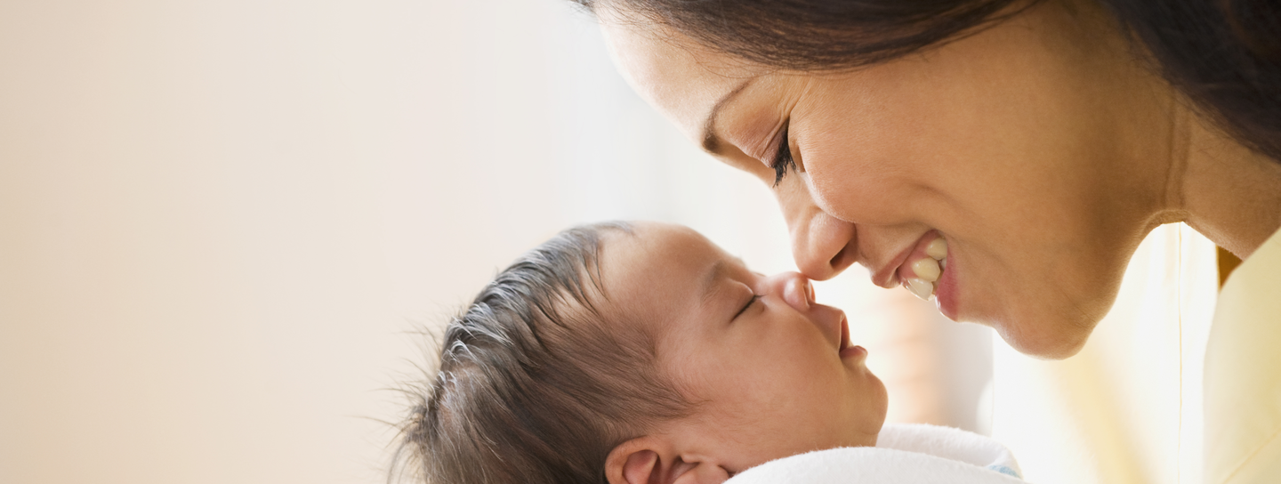 A mother leans down, nose to nose with her wrapped baby