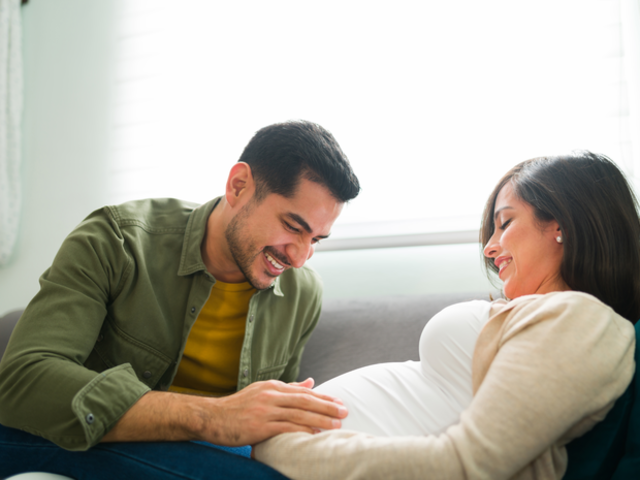 A pregnant couple sits together in bed.