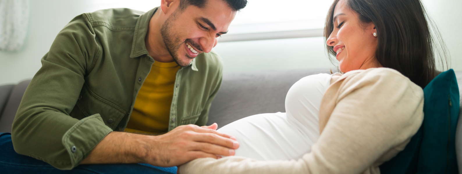 A pregnant couple sits together in bed.