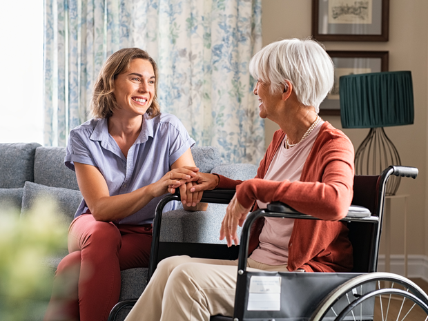 Woman holds hands with elderly loved one in wheelchair.