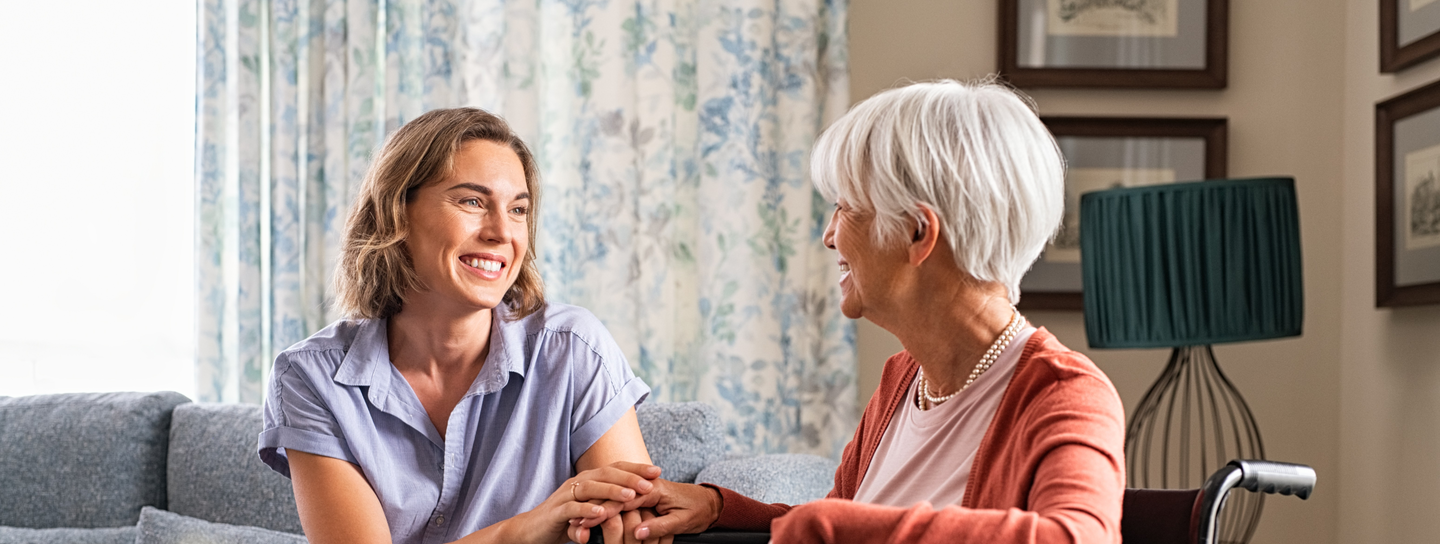Mature woman comforting senior mom sitting on wheelchair at home. 