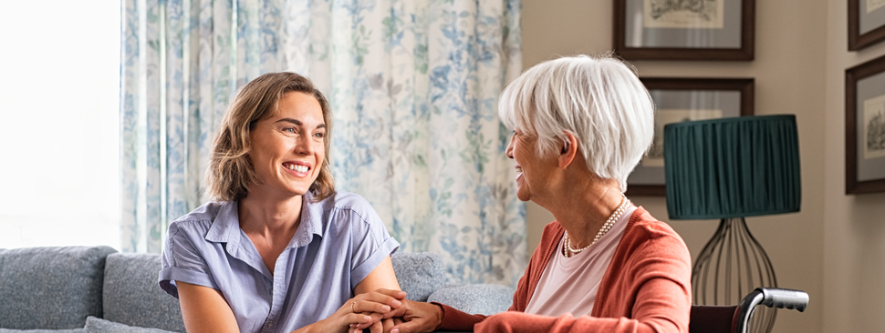 Mature woman comforting senior mom sitting on wheelchair at home. 