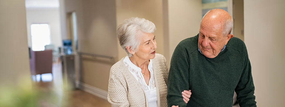 Senior woman helping husband walk at medical clinic