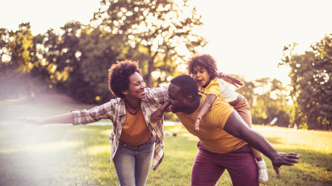 Family of three smiles and plays outdoors at sunset.