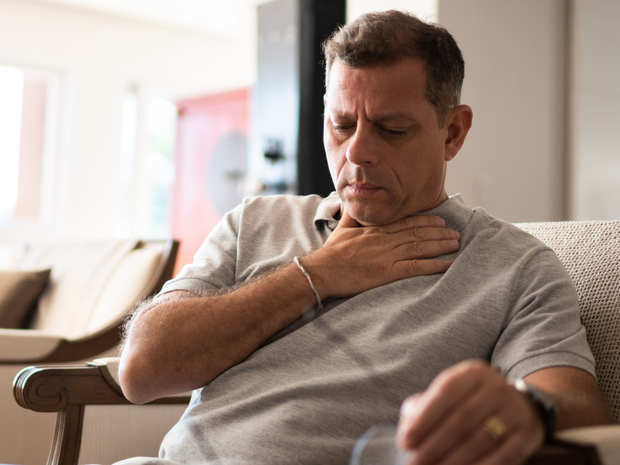 Man with cold holds throat in discomfort.