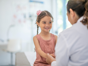 A girl of elementary age sits on the examination table while being seen by her doctor.