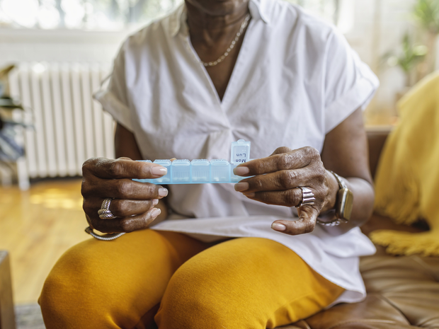 Women sitting on a couch holding a pill organizer.
