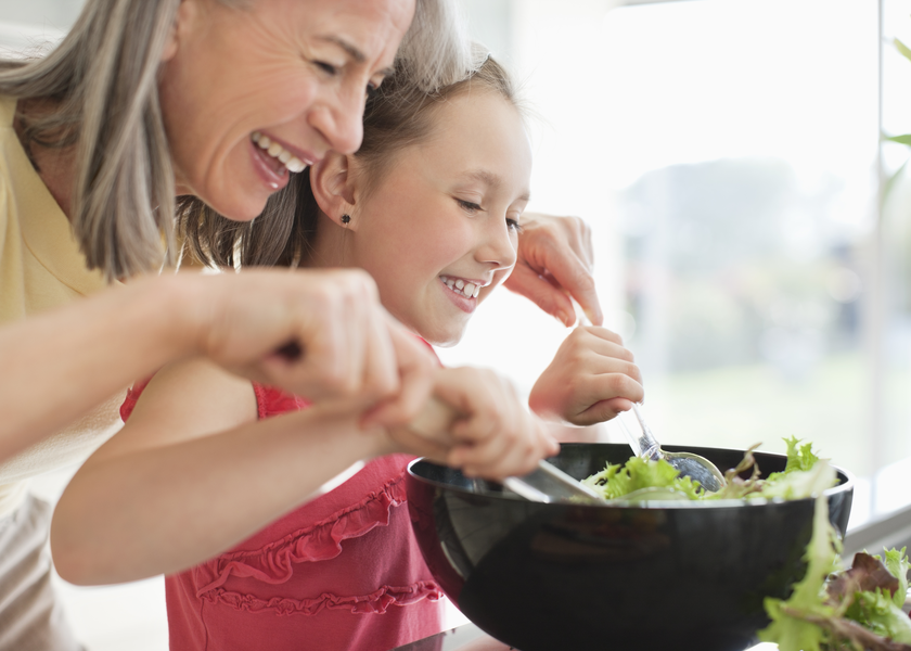 A grandmother helps her grandchild mix a salad in a bowl