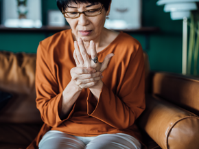 Older woman grabs hand in pain on sofa.
