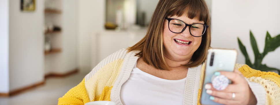 A woman sits on the couch at home, laughing at her phone