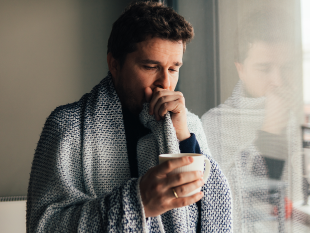 man coughing wrapped in a blanket