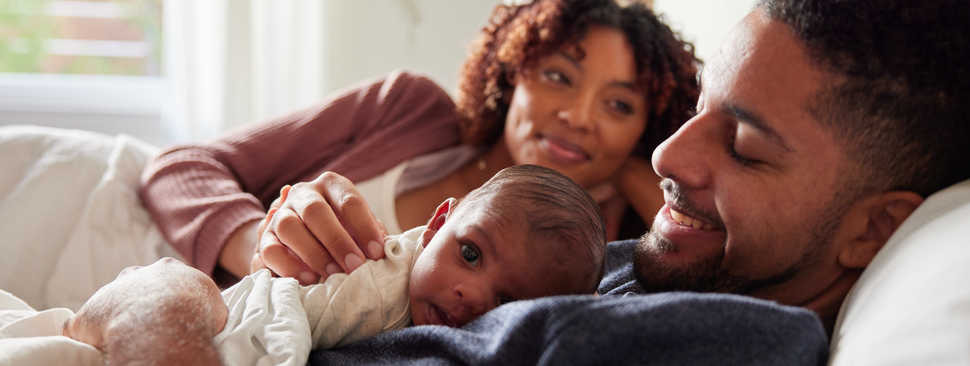 Smiling mom looking at her husband and baby lying in bed