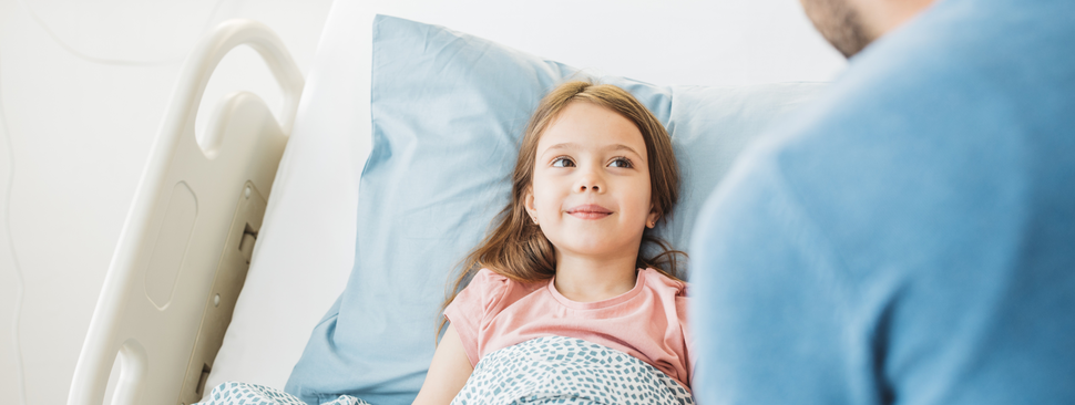 A little girl laying in a hospital bed in a pink shirt surrounded by a doctor and her mom.