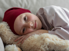 Young patient with head scarf cuddles stuffed animal.
