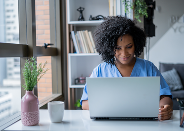 Provider in scrubs works on laptop.