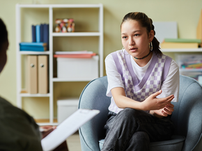 A teenager sits, seriously talking to an adult across from her