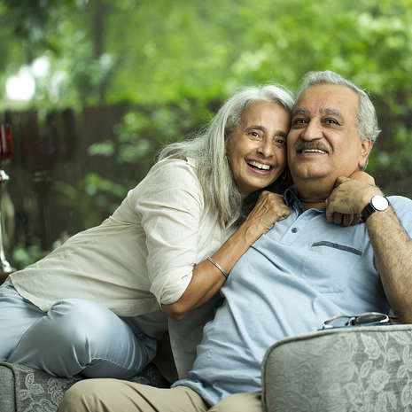 Senior woman lays her head on her husband’s shoulder while relaxing together at home