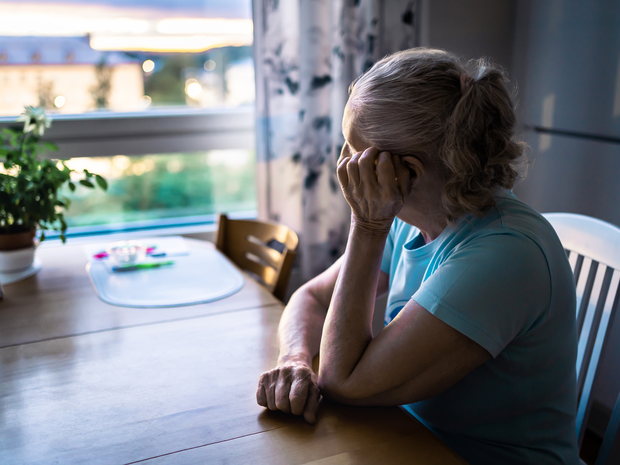Elderly woman looks out her window.