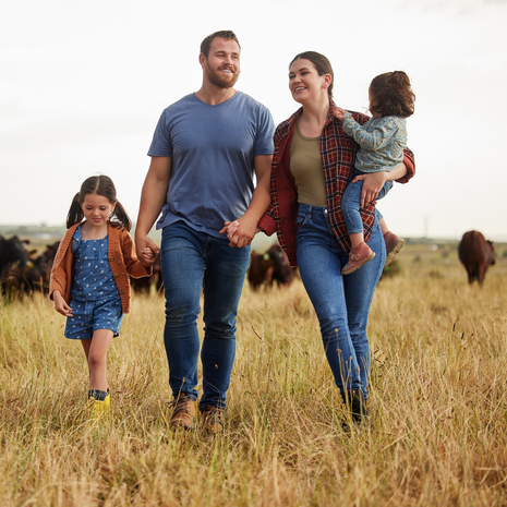 Happy family with young kids walking through a field with cattle