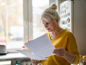 Woman looks at her bill while in her kitchen