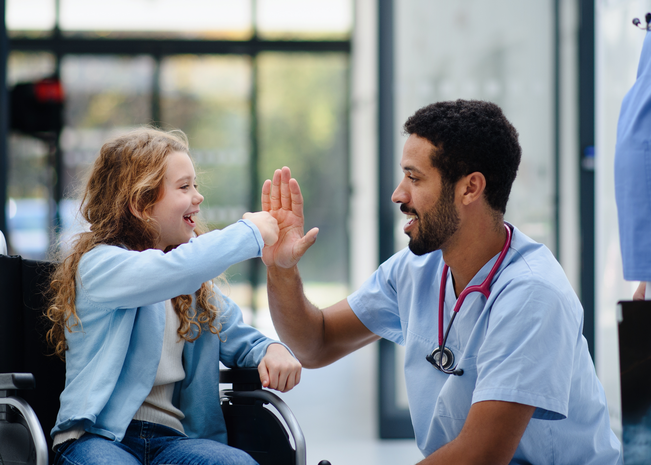 Girl in wheelchair smiles and high fives her provider.
