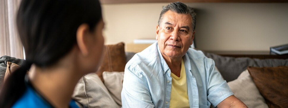 Senior man sitting and talking with female nurse in blue scrubs