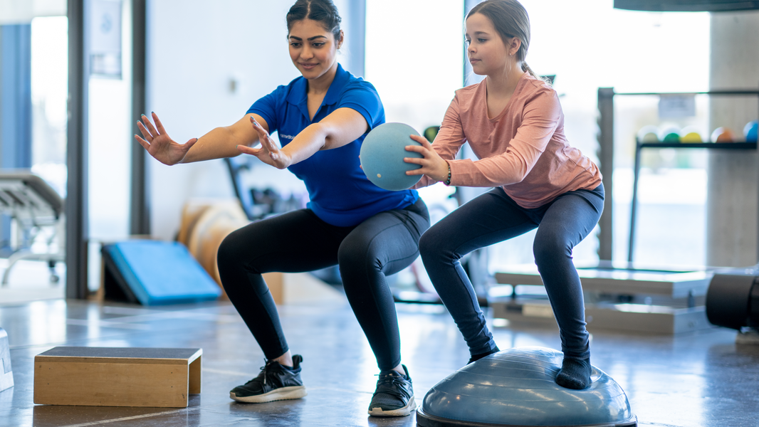 Young girl does squats on medicine ball.