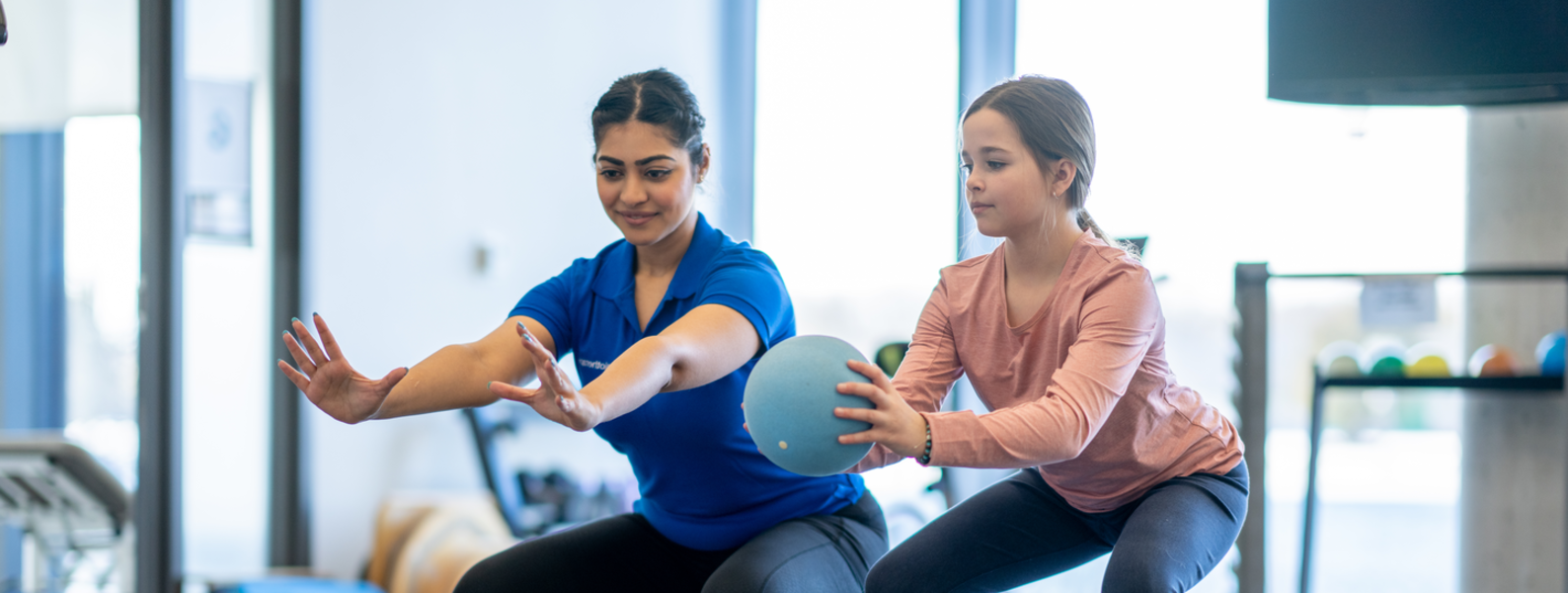 Young girl does squats on medicine ball.
