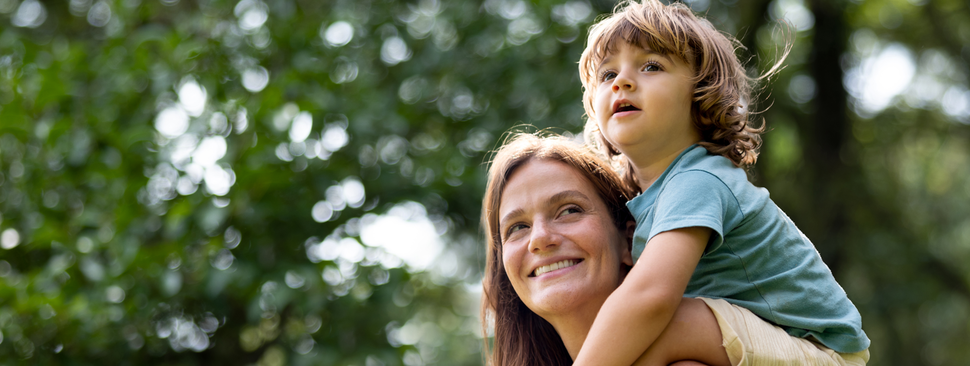 Happy mother carrying her son on her shoulders at the park