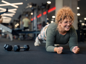 Determined smiling young woman with curly hair in plank position