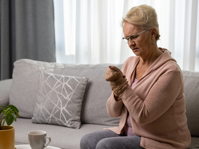 Older woman grabs hand in pain on sofa.