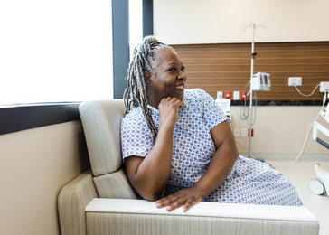 A woman wearing a hospital gown sits on a couch in a hospital room