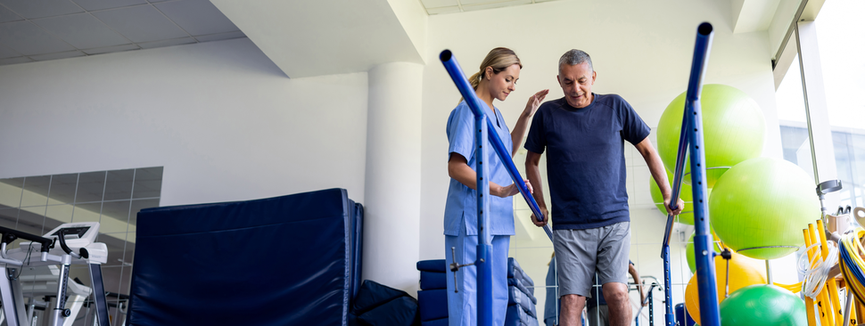 Man recovering from an injury and walking on bars with the assistance of his physical therapist