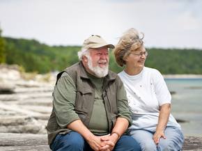 A senior couple sitting on some large shore rocks, looking out towards the water.