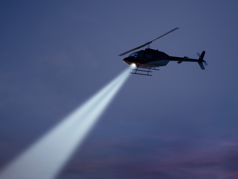 Helicopter flies with spotlight on at night.