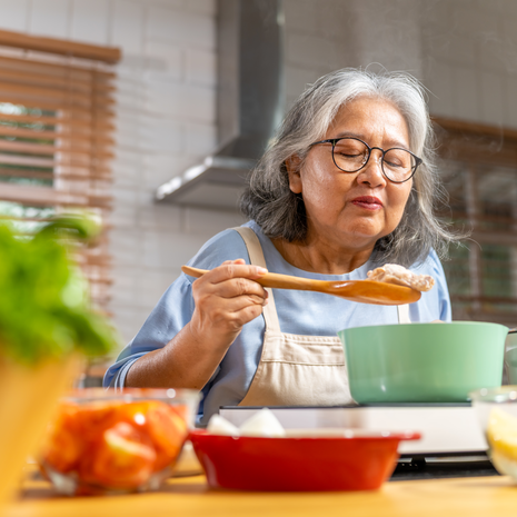 senior woman cooking chicken soup with vegetables on kitchen island counter