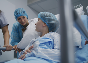 A child on a hospital bed looks back at her mother as she's wheeled through the hallway