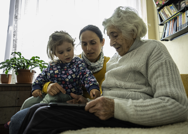Elderly woman reads book with daughter and granddaughter.