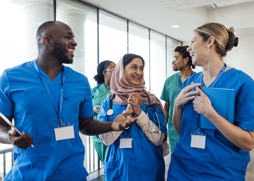 A trio of doctors in scrubs walk through the hallways while laughing happily
