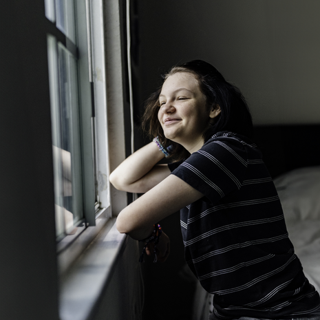 Non binary teenager looking out bedroom window