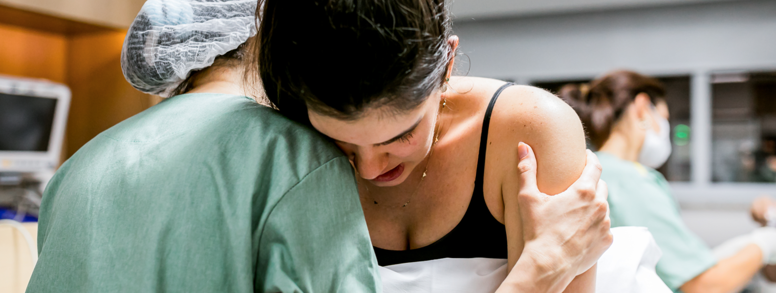 A woman in labor rests her head on the shoulder of a medical professional aiding her