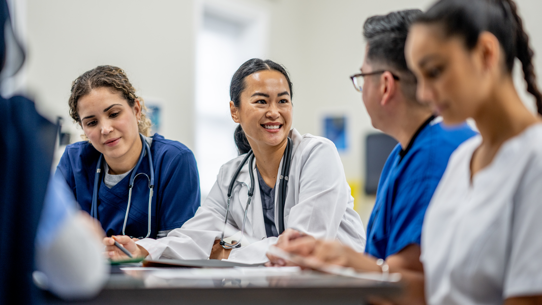 Providers smile while meeting at a table in a hospital.