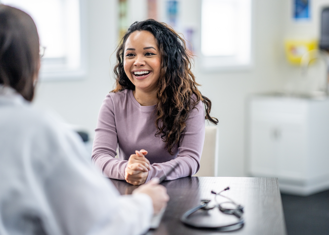 A woman in a purple shirt smiles at a health professional across from her