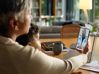 Mother on a virtual care appointment with her son on her lap