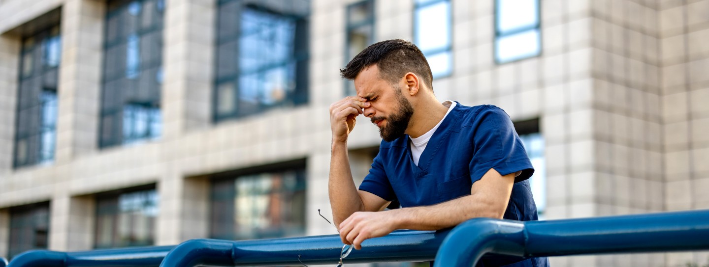 Nurse in deep thought leaning on metal railing outside of work