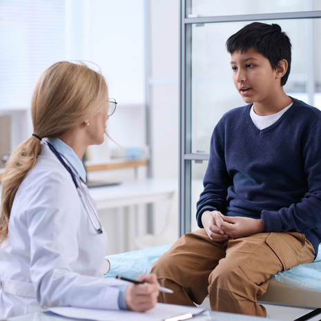 Portrait of young boy talking to doctor in clinic.