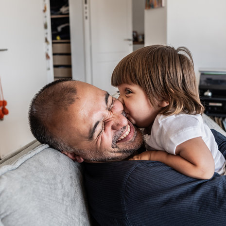 A father plays with his toddler daughter on the sofa.