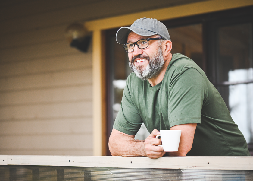 A man leans over his deck with a cup of coffee