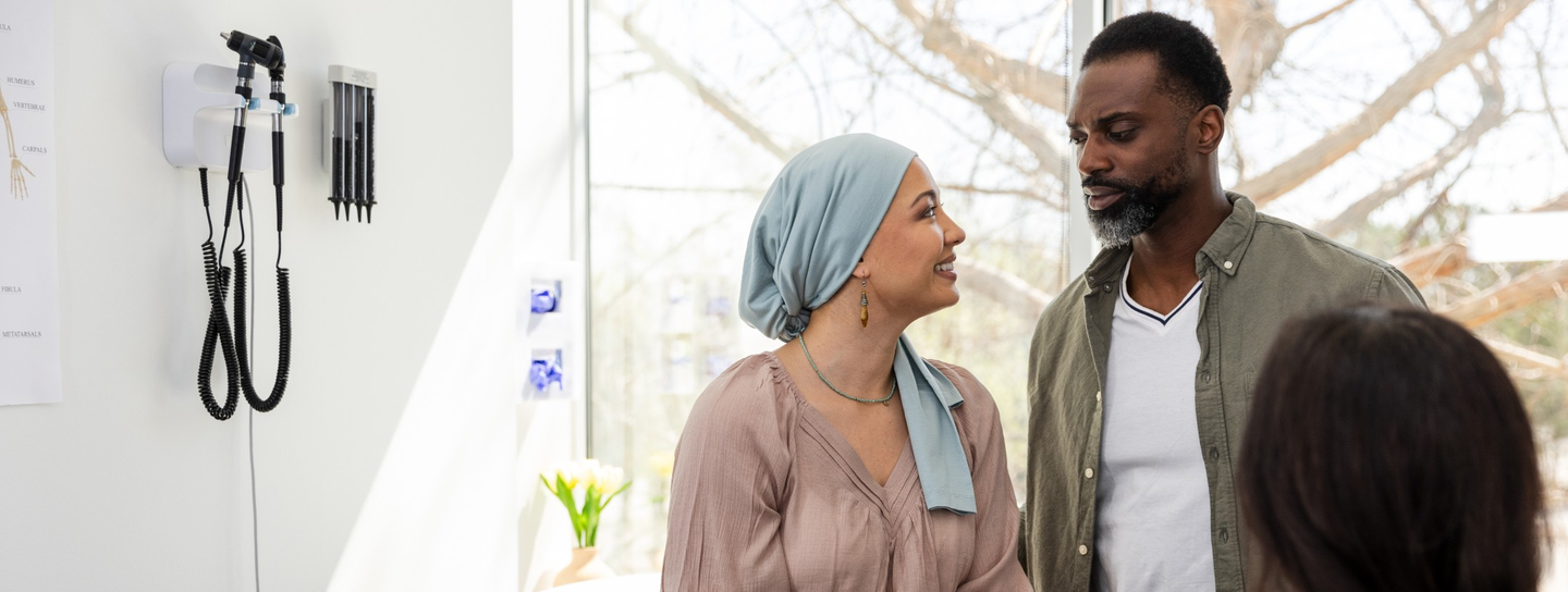 A woman in a head scarf looks up at her husband in a hospital setting