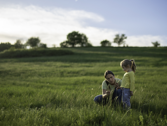 Mother and young daughter talking in a field.